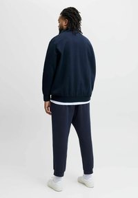 Marinblå sweatshirt med elastiska mudd och nederkant, matchad med avsmalnande sweatpants. Vit lagertröja under och vita sneakers.
