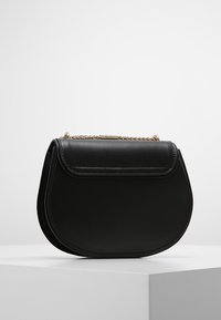 Musta nahkainen käsilaukku, jossa on kaartuva muoto, läppäkiinnitys ja kultainen ketjuhihna. Sileä pinta, jossa yksinkertaiset ompeluaiheet.