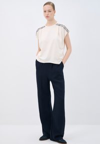 Blouse en crème avec des embellissements texturés aux épaules, accompagnée de pantalons large bleu marine. Tissu doux, coupe décontractée, avec des poches latérales.
