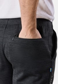 Svarta atletiska joggers med en texturerad tyg, med en blixtlåsficka på sidan och en liten accentflagga på benet.