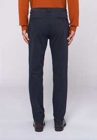 Mörkblå byxor med rak benlängd, med två bakfickor och bälteshällor, tillverkade av ett slätt bomullsmaterial.