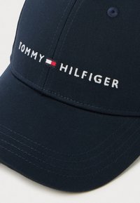 Navy baseball cap made of textured fabric, featuring white embroidery of "TOMMY" and "HILFIGER," with a red and white accent stripe.