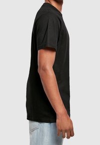 Schwarzes Baumwoll-T-Shirt mit kurzen Ärmeln und Rundhalsausschnitt, seitlich gezeigt, kombiniert mit hellblauen Jeans.