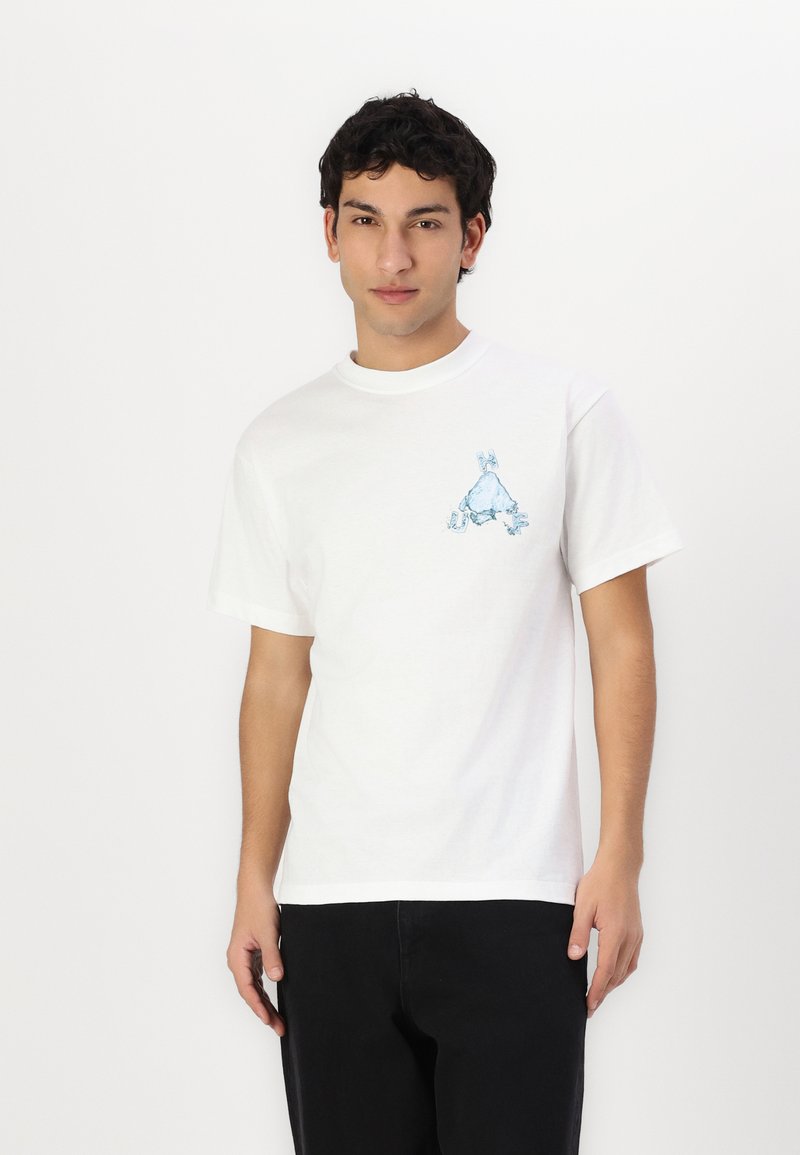 Baltos medvilnės marškinėliai trumpomis rankovėmis. Kairėje krūtinės pusėje yra mėlyna grafika. Modelis dėvi juodas kelnes.