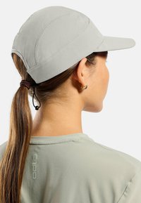 Light gray cap with a curved brim, textured fabric, and adjustable toggle at the back. Worn with a matching light gray shirt.