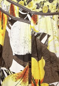 Żółta, brązowa i biała tkanina w kwiaty z abstrakcyjnymi wzorami liści i płatków, ozdobiona brązowymi liniami ściegów i marszczonymi zakładkami.