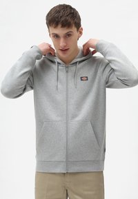 Gray zip-up hoodie made of soft fabric with a front pocket, drawstrings, and a small logo patch on the left chest.