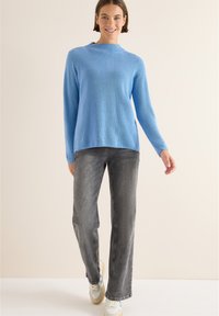 Helles blaues, geripptes Strickoberteil mit hohem Kragen. Kombiniert mit grauen, weiten Jeans und weißen Sneakers mit blauen Akzenten.