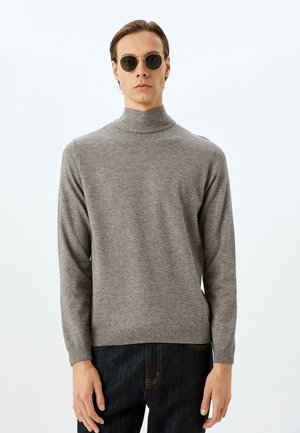 Suéter gris de cuello alto con canalé y mangas largas, hecho de material suave. Combinado con jeans oscuros, presenta un dobladillo recto. Gafas de sol circulares.