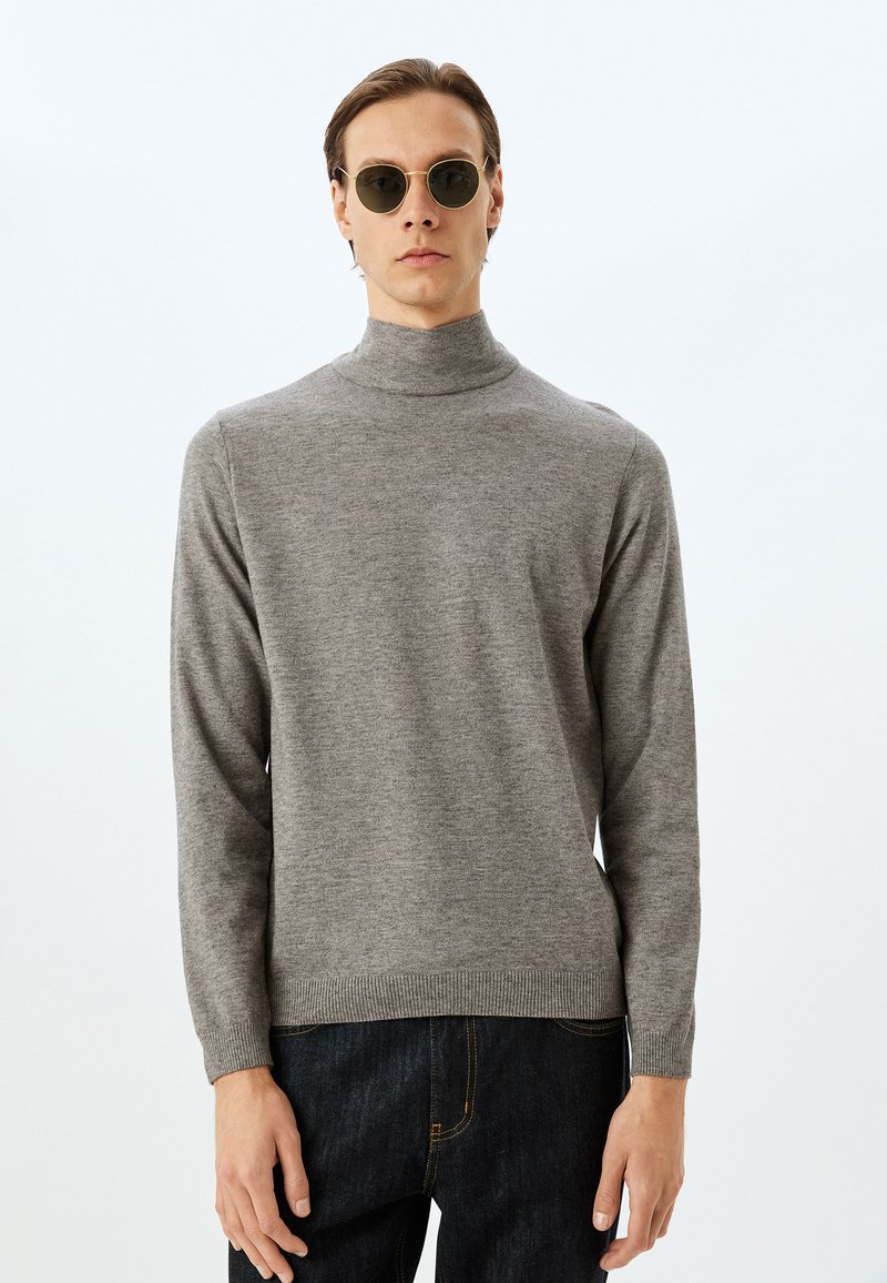 Grå, ribbad polotröja med långa ärmar, gjord av mjukt material. Buren med mörka jeans, har en rak avslutning. Runda solglasögon.