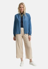 Chemise bleu clair à boutons avec des épaules froncées, associée à un pantalon large crème et des baskets blanches. Texture de tissu lisse.