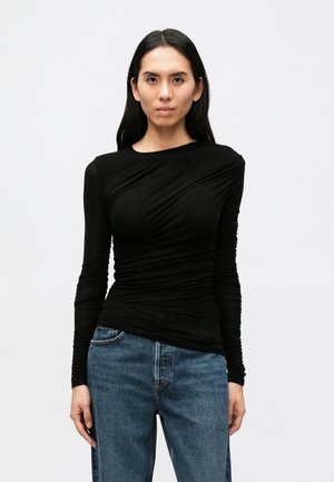 Top preto de manga comprida com detalhe de tecido drapeado, design ajustado e textura suave, combinado com jeans azuis folgados.