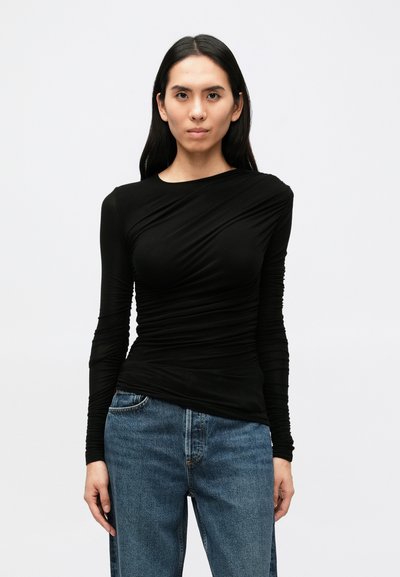 Top nero a maniche lunghe con dettaglio in tessuto drappeggiato, design aderente e tessuto liscio, abbinato a jeans di denim blu a taglio largo.