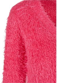 Gros plan d’un tissu texturé duveteux rose vif montrant des fibres douces en boucle couvrant une manche et une épaule de vêtement.