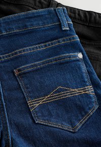 Két pár farmer: az egyik sötétkék denim, narancssárga varrással és egy hátulsó zsebből álló dizájnnal; a másik fekete, sima textúrával.