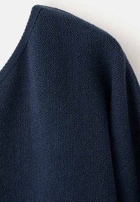 Nachtblaue, strukturierte Strickjacke mit weichem, gewebtem Aussehen und entspannter Silhouette, mit einem weiten Ausschnitt und minimalen Nahtdetails.
