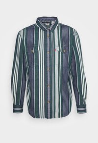 Camisa de botón con rayas verticales en verde oscuro, azul marino y blanco. Presenta dos bolsillos en el pecho y botones metálicos. Textura suave.