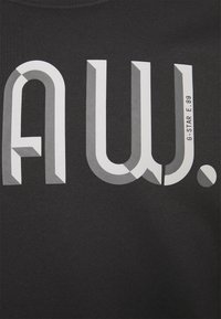 Tissu noir avec des lettres blanches et grises en style 3D audacieuses formant "A W." et un petit texte "G-STAR E.89" sur le côté droit.