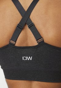Sujetador deportivo negro con diseño de espalda cruzada, tirantes ajustables y un acabado texturizado, marcado con el logotipo blanco "ICIW".