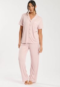 Set di pigiama rosa chiaro composto da una maglietta a maniche corte con bottoni e tasca, abbinata a pantaloni lunghi. Tessuto morbido con dettagli in bianco.