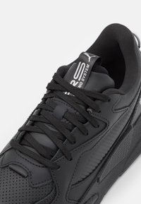 Baskets noires avec une tige en cuir lisse, accents texturés contrastants et lacets noirs. Présentent un logo sur la languette et des détails perforés.