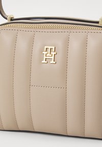 Bež torba od kože s horizontalnim kviltanim uzorkom, zlatnim hardverom i istaknutim reljefnim logotipom.