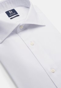 Balta krekla ar gludu audumu, standarta apkakle, priekšējie pogas un maiga tekstūra. Zīmola etikete pie apkakles.