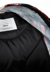 Interior de una mochila con un suave forro de tela negra y un diseño multicolor en el lado opuesto, que muestra varios patrones gráficos.