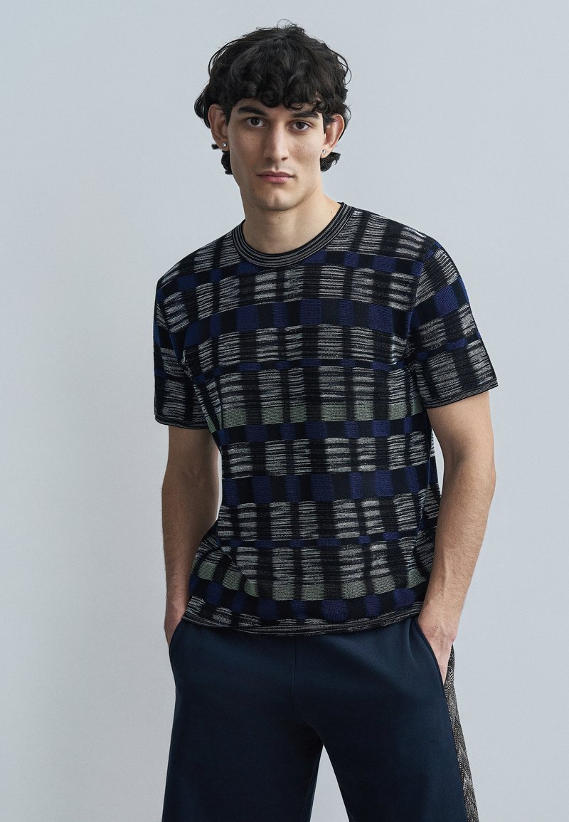 Κοντομάνικη πλεκτή μπλούζα με σχέδιο σε μαύρο, μπλε και πράσινο. Διαθέτει στρογγυλή λαιμόκοψη και άνετη εφαρμογή. Μαλακή υφή.