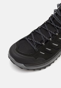 Czarne buty sportowe z teksturowaną cholewką, solidną gumową podeszwą, odblaskowymi akcentami oraz lekką konstrukcją z wzorzystymi sznurowadłami.