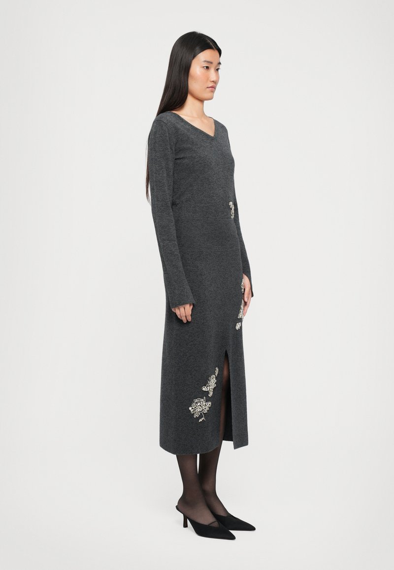 Langes, enges graues Strickkleid mit V-Ausschnitt, langen Ärmeln, wadenlanger Länge, seitlichem Schlitz und silbernen floralen Stickdetails.