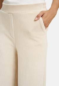 Beige gerippte weite Hosen mit weicher Textur, ausgestattet mit einem glatten Bund und seitlichen Taschen für zusätzlichen Komfort.