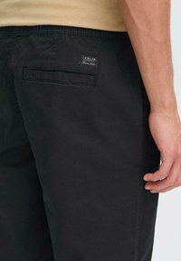 Pantalones de mezcla de algodón negros con una textura suave, que cuentan con un bolsillo trasero y una etiqueta de marca, diseñados con una cintura elástica para mayor comodidad.