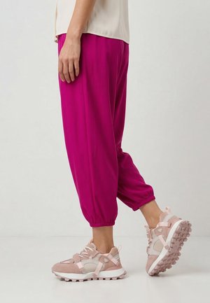 Person wearing bright pink jogger pants and beige-pink chunky sneakers, standing sideways on a plain light background.