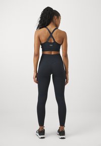 Sostén deportivo azul marino con tirantes cruzados y logo, combinado con leggings texturizados de cintura alta. Zapatillas deportivas negras completan el conjunto.
