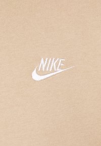 Logo Nike blanc brodé et swoosh sur fond en tissu beige tricoté.