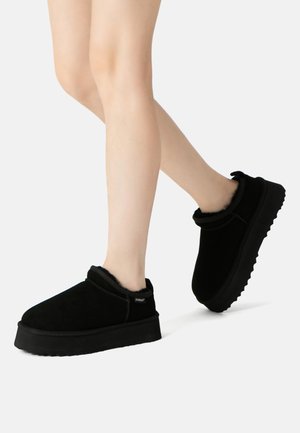 Black suede slip-on shoes with a plush interior, rubber sole, and subtle stitching details, featuring a low platform design.