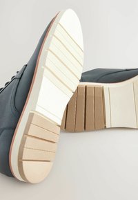 Blue leather shoes with a white, textured sole featuring horizontal grooves and a slightly raised heel. Accents include contrasting stitching.