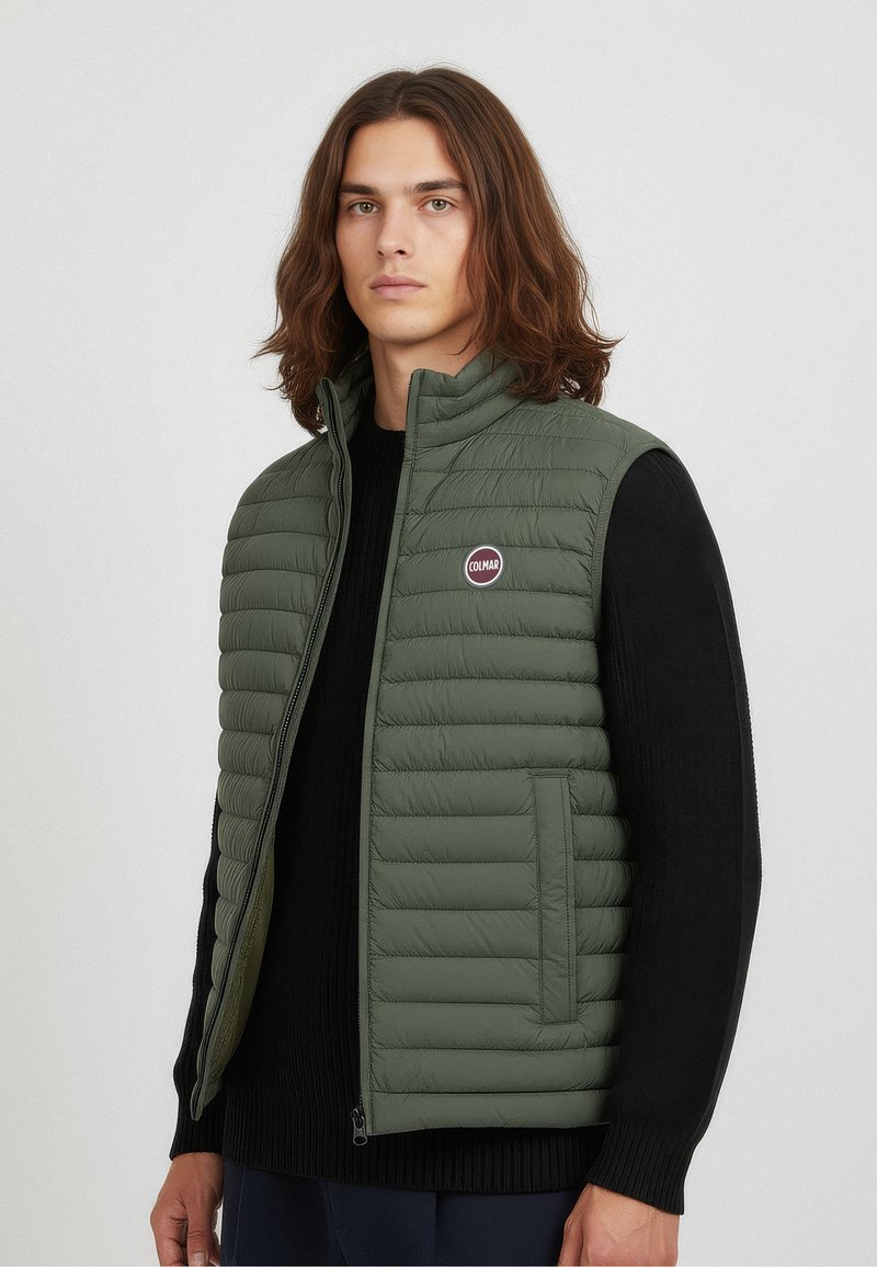 Lightweight green puffer vest with horizontal stitching, high collar, and logo detail. Paired with a black knitted sweater underneath.