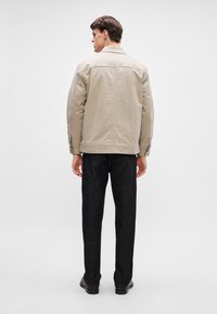 Beżowa kurtka z wyraźnym kołnierzem, z przodu na guziki i dwoma bocznymi kieszeniami; zestawiona z ciemnoniebieskimi dżinsami i czarnymi butami. Minimalistyczny design.