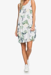 Robe blanche sans manches ornée de motifs de feuilles tropicales vertes et de fleurs. Coupe ample, longueur aux genoux, en tissu léger. Associée à des baskets blanches.