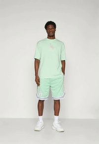 Γυμναστική σετ σε μέντα πράσινο χρώμα που περιλαμβάνει μπλουζάκι κοντομάνικο με λογότυπο και αντίστοιχες σορτς με λευκές αντίθετες λεπτομέρειες και γραφικά στοιχεία.