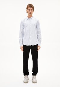 Chemise boutonnée à rayures bleu clair et blanches, pantalon noir et baskets argentées. La chemise a un col classique et une coupe décontractée.