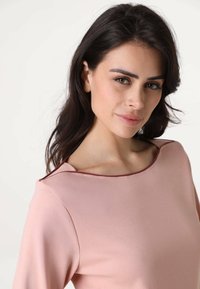 Top rosa pallido con scollatura rotonda, maniche corte e una texture del tessuto liscia. Presenta una rifinitura a contrasto lungo la scollatura.