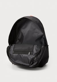 Sac à dos en nylon noir avec un design courbé, doté d'une poche en maille zippée à l'intérieur. L'intérieur est lisse avec un seul compartiment principal.