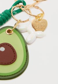 Avokado-muotoinen avaimenperä vihreästä ja ruskeasta nahasta, jossa on kultainen avainrenka, vihreä naru, ilmapallokoira-riipus ja sydänmerkki.