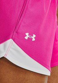 Rosa träningsshorts med texturerad tyg, vit fåll och kontrasterande vita sömmar. Har en liten vit logotyp nära botten.