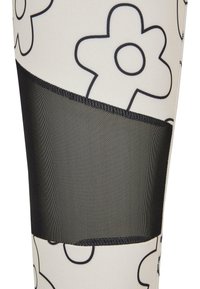 Leggings med hvit base med svarte blomstmønstre, supplert med et svart mesh-panel ved kneet for ekstra tekstur og detaljer.