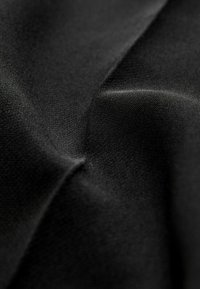 Černá tkanina s hladkým povrchem, vykazující jemné sklady a jemný vzor tkaní, zdůrazňující její monochromatickou barvu a hloubku.