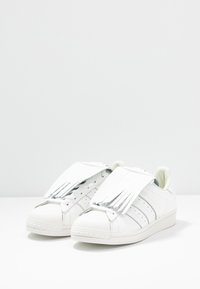 Vita sneakers med ovandel i läder, med fransiga detaljer på tungan, rund tåhuvud och perforerade sidosträck. Platta snören ingår.